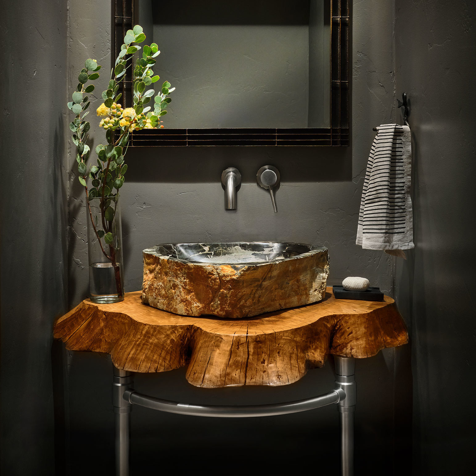 A Jamestown style Vanity Leg System in satin nickel supporting a "live edge" slab table from a tree trunk with a marble vessel basin
