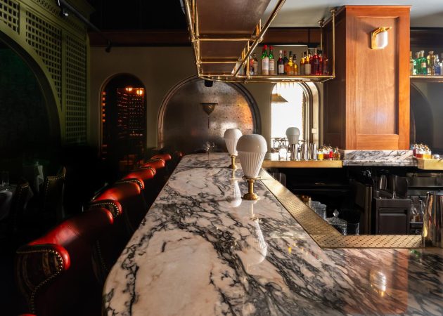 Bar featuring wood ceiling mounted bottle shelf supported by curved brass tubing with Ball style fittings