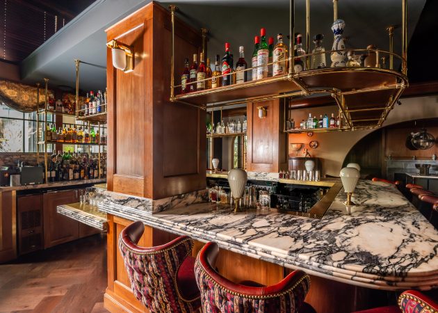 Bar featuring wood ceiling mounted bottle shelf supported by curved brass tubing with Ball style fittings