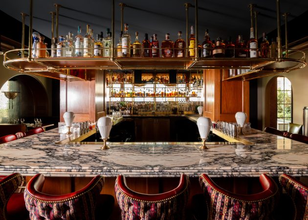 Bar featuring wood ceiling mounted bottle shelf supported by curved brass tubing with Ball style fittings