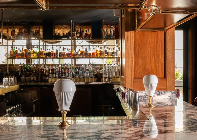 Bar featuring wood ceiling mounted bottle shelf supported by curved brass tubing with Ball style fittings