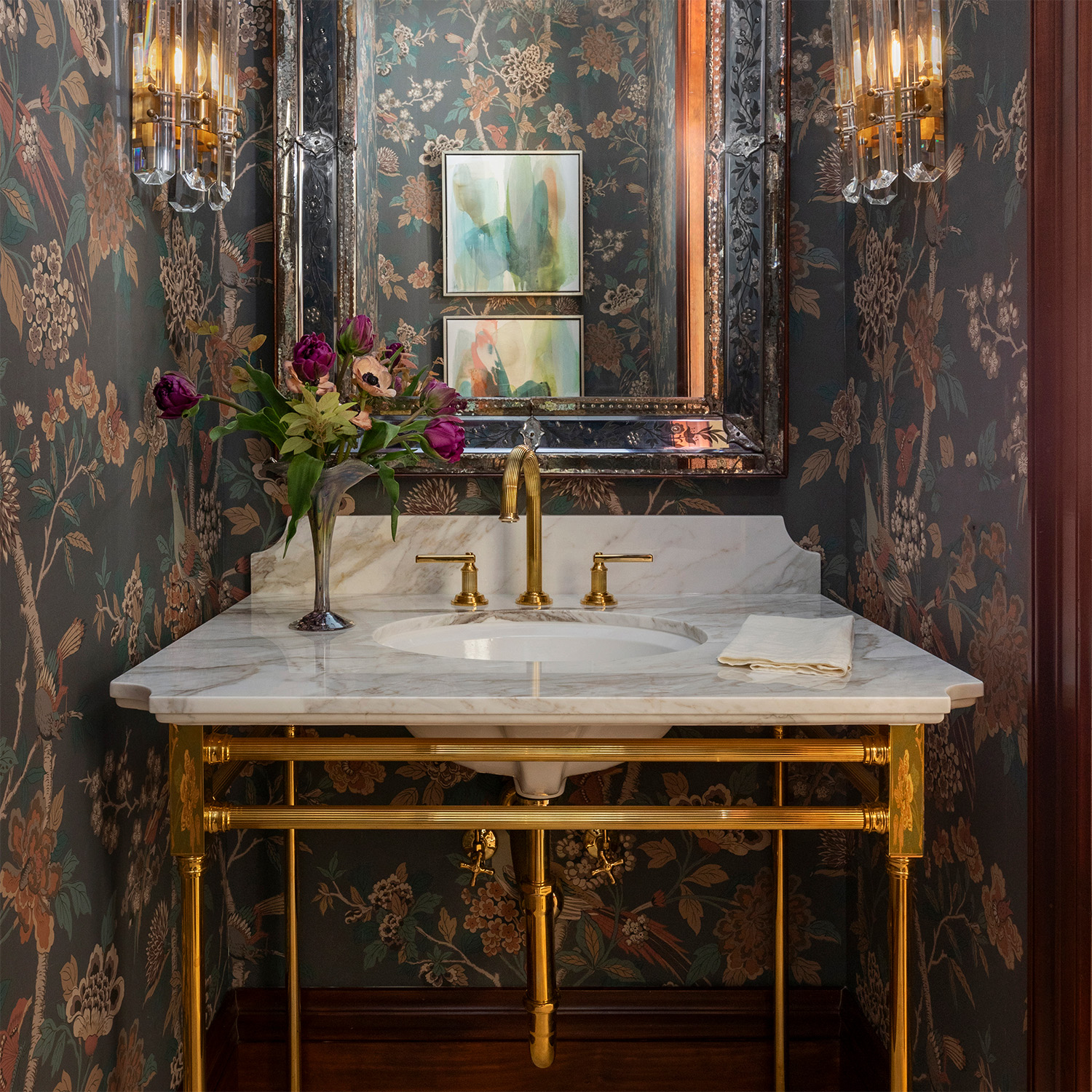Capital style vanity in polished brass with marble top in elegant bathroom with floral wallpaper